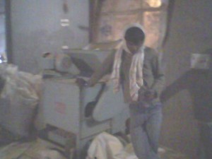 करावलनगर के एक गोदाम में बादाम तोड़ने की मशीन के साथ खड़ा मज़दूर